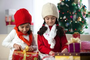 two young girls opening presents in front of a christmas tree